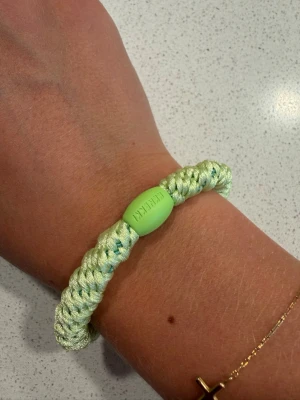 Kknekki hårband  - Snyggt ljusgrönt armband med flätad design och en oval pärldetalj i plast där det står 'RAKETEN'. Tillverkat i glansigt syntetmaterial som ger en cool och modern look. Perfekt accessoar för att lyfta din outfit.