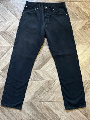 Levi's 521 - Säljer ett par svarta jeans från Levi's med klassisk rak passform. Jeansen har fem fickor, silverfärgade nitar och Levi's ikoniska läderpatch bak i midjan. Materialet är kraftig denim som ger en tidlös look.Längd 104cm Bredd 39cm
