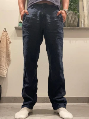 Mörkblå linnebyxor med rak passform - Säljer ett par mörkblå linnebyxor med rak passform och avslappnad look. Byxorna har sidfickor och resår i midjan för extra komfort. Perfekta för dig som gillar en chill och stilren vibe. Materialet är luftigt linne som passar bra till varmare dagar.