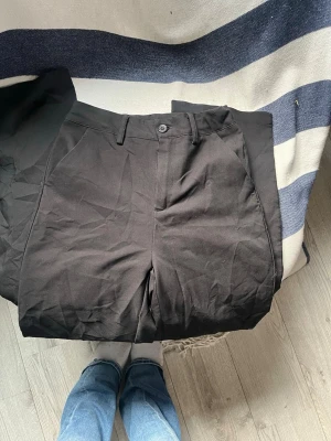 Svarta kostymbyxor med raka ben - Snygga svarta kostymbyxor med raka ben och klassisk passform. Byxorna har hällor för bälte, snedställda fickor fram och två passpoalfickor bak. Materialet ser ut att vara en bomulls- eller polyestermix som ger en stilren look.