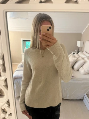 Beige stickad tröja med rund hals - Mysig beige stickad tröja med rund halsringning och långa ärmar. Tröjan har en enkel och stilren design med ribbstickade muddar vid ärmslut och nederkant. Tröjan har ett hål vid ena ärmen, vilket säkert går att sy ihop💗