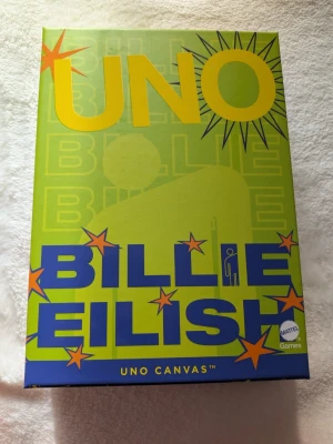 Billie Eilish UNO Canvas - Helt nytt och oöppnat - Billie designed this blohsh-filled UNO Canvas Billie Eilish deck featuring colors, symbols and numbers that showcase her artistic aesthetic, printed on 300-gram premium card stock. Deal yourself in for an epic game night, and don't forget what you're supposed to do when you get down to your last card.  - UNO Canvas™ Billie Eilish - 112 premium-quality cards and instructions in a set-up box - Deck features Billie's Blohsh logo integrated playfully throughout - Package dimensions: 5.000" W x 7.000