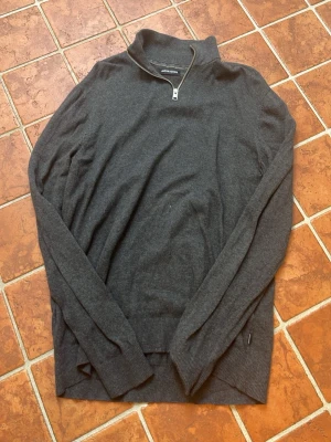 Mörkgrå halvzip tröja Jack & Jones - Mörkgrå stickad tröja från Jack & Jones med halvzip och hög krage. Tröjan har långa ärmar, ribbade muddar och är tillverkad i mjukt material. Väldigt bra skick och pris kan diskuteras 