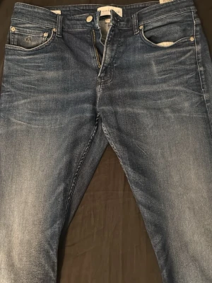 Blå jeans med slitningar - Säljer ett par klassiska blå jeans med snygga slitningar och tvättad look. Jeansen har fem fickor, normal midja och raka ben. Materialet är denim som ger en skön och avslappnad känsla. Perfekta till vardags för en cool och enkel stil. ( Jeansen är slim fit) Storlek W33 L34. Anledningen till att jag säljer dom är för att de var lite för långa enligt mig, är 178! 