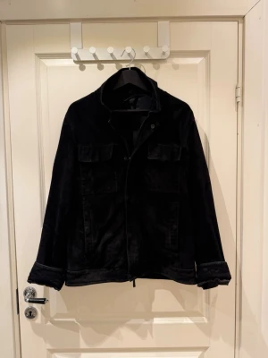 Massimo Dutti Svart manchesterjacka  - Snygg svart manchesterjacka med klassisk krage och två bröstfickor med lock. Jackan har långa ärmar och stängs framtill med knappar. Perfekt för dig som vill ha en stilren och tidlös look.