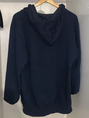 Mörkblå hoodie från Comme des Garçons - Snygg mörkblå hoodie från Comme des Garçons PLAY med dragkedja framtill och justerbar huva. Klassisk design med diskreta detaljer och mjukt material som känns skönt mot huden. Priset kan lätt diskuteras vid snabbaffär 