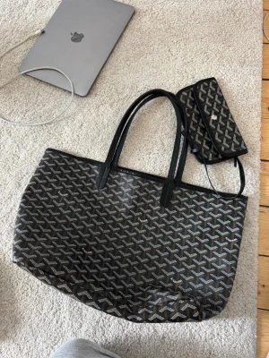 Svart shoppingväska med mönster - Stilren väska med rutigt mönster och en medföljande plånbok. Se sista bild för skick. använd och i mycket fint skick, dustbag medföljer även. Hör gärna av dig vid frågor!