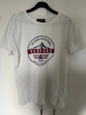 Vit t-shirt med Redford-tryck - Vit t-shirt från Redford med rund hals och tryck framtill som har texten 'Outdoor Adventures' och 'Mountain Explorer' samt bergmotiv. T-shirten är kortärmad och gjord i mjuk bomull, perfekt för en avslappnad stil. Bra skick 