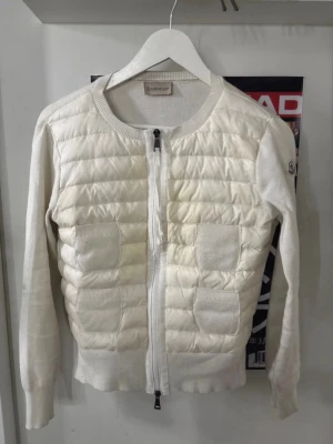 Vit moncler cardigan - Jag säljer min vita moncler cardigan, den har lite fläckar här och där men ska såklart tvättar innan! Den är äkta och Qr koden skannas, bara att skriva om ni vill ha en bild på det! Den har inga skador och är i bra skick, loggan på armen har också en scanning. Bara att skriva om ni har frågor, mappen följer såklart med! Passar storlek S-M. ❗️Den är inne på kemtvätt just nu så den kommer vara mer vitare❗️