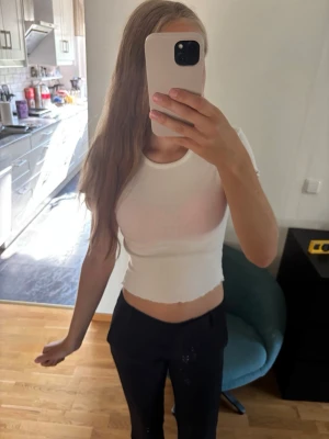Vit ribbad crop top med vågig kant - Säljer en vit ribbad crop top med korta ärmar och vågig kant nertill. Toppen är figurnära och har en stretchig passform som sitter snyggt på kroppen. Perfekt att matcha med jeans eller kjol för en trendig look. Toppen är använd ca 3 gånger men inga skador, precis som ny!
