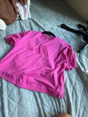 Rosa loose-fit t-shirt - En rosa t-shirt i loose-fit modell med korta ärmar och rund hals. T-shirten är enkel och stilren utan synligt tryck eller logga, perfekt för en avslappnad look. Materialet ser ut att vara mjukt och bekvämt, troligtvis bomull.
