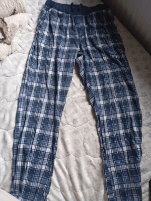 Rutiga blå pyjamasbyxor - Säljer ett par klassiska pyjamasbyxor i blått och vitt rutigt mönster. Byxorna har resår i midjan och är tillverkade i ett mjukt, tunt tyg som känns skönt mot huden. Perfekta för slappa dagar hemma eller mysiga kvällar. Pris kan diskuteras vid snabb affär🙌. Mvh Rasmus.