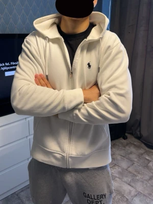 Vit zip hoodie från Polo Ralph Lauren - Säljer en fräsch vit hoodie med dragkedja från Polo Ralph Lauren. Klassisk design med huva och dragsnören, två fickor framtill och den ikoniska lilla loggan broderad på bröstet. Perfekt till chill eller streetwear-stil.