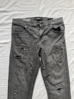 Svarta replay jeans  - Säljer ett par svarta jeans med slitningar på framsidan och klassisk femficksdesign. Jeansen har smal passform och är tillverkade i bomull med en liten mängd stretch för extra komfort. Perfekta för en trendig och avslappnad stil.