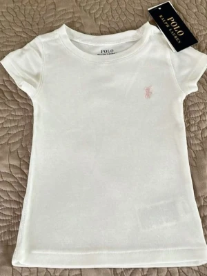 Vit t-shirt från Polo Ralph Lauren - Klassisk vit t-shirt från Polo Ralph Lauren med korta ärmar och rund hals. T-shirten har en liten rosa broderad logga på bröstet och är gjord i mjuk bomull för en skön känsla. Perfekt basplagg till garderoben.