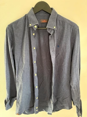 Blå skjorta från Morris - Klassisk blå oxfordskjorta från Morris med button-down krage och broderad logga på bröstet. Skjortan har långa ärmar, vita knappar och är tillverkad i mjukt bomullstyg. Perfekt för en stilren och avslappnad look.