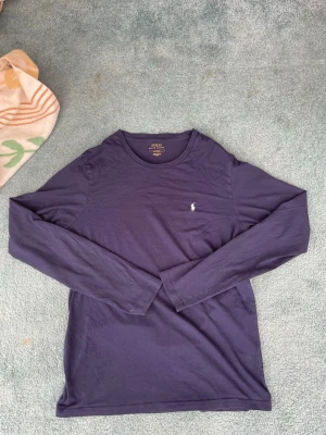 Mörkblå långärmad tröja Polo Ralph Lauren - Snygg mörkblå långärmad tröja från Polo Ralph Lauren med rund halsringning och den klassiska vita logon broderad på bröstet. Tillverkad i mjuk bomull som känns skön mot huden. 
