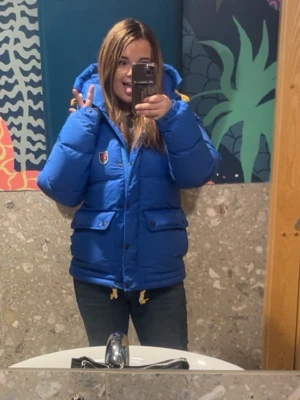 Blå dunjacka från Fjällräven - Säljer en blå dunjacka från Fjällräven med huva och två stora fickor framtill. Jackan har dragsko i nederkant och klassisk Fjällräven-logga på bröstet. Perfekt för kalla vinterdagar och riktigt varm tack vare dunfyllningen. Använt 1 vinter säsong sen inget mer så är nästan ny då av priset!
