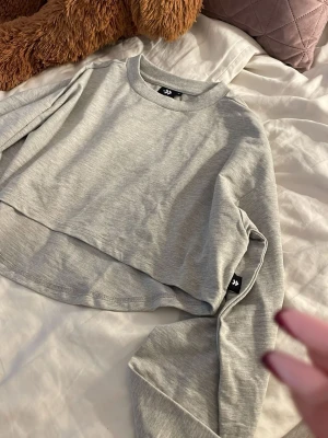 Ljusgrå cropped hoodie - Säljer en ljusgrå cropped hoodie med rund hals och långa ärmar. Hoodien har en enkel och clean design utan tryck eller dragkedja. Tillverkad i mjukt sweatshirtmaterial som är skönt mot huden. Perfekt till jeans eller mjukisbyxor.