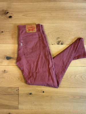 Levi’s 511  W31 L32 - Ovanligt snygga Levi’s 511 i tegelröd/vinröd färg - en riktig blickfångare för den som vill sticka ut från mängden. Slim fit med rak passform nertill, klassisk femficksmodell med nitar och äkta läderlapp.  Detaljer:  	•	Modell: Levi’s 511 	•	Storlek: W31 L32 	•	Skick: Använt skick - : en större fläck på vänster ben  	•	Färg: Tegelröd/vinröd - ovanlig och trendig nyans 	•	Äkta läderlapp och röd Levi’s-etikett på bakfickan 	•	Nitade fickor fram