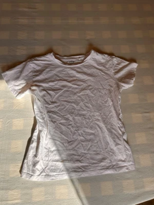 Vit basic t-shirt i bomull - En enkel vit t-shirt i mjuk bomull med rund hals och korta ärmar. Perfekt till jeans eller shorts och funkar året runt. Klassisk passform och stilren design utan tryck eller detaljer.