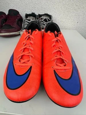 Nike fotbollsskor - Säljer ett par snygga fotbollsskor från Nike i en stark röd färg med stora blå swoosh-loggor på sidorna. Skorna har snörning, låg profil och svart kant runt öppningen. Perfekta för dig som vill sticka ut på planen! Grym skick och bra pris! In o köp!
