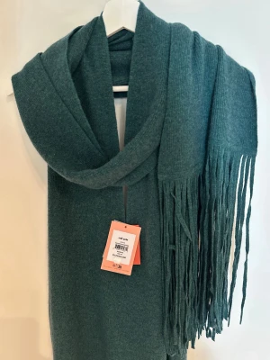 Cult Gaia Jorden klänning Seamoss – merinoull & kashmir – M - Helt ny Cult Gaia Jorden klänning i färgen Seamoss, storlek M. Lapparna sitter kvar.  Lyxig stickad modell i en mjuk blandning av merinoull och kashmir. Klänningen har en elegant draperad halsringning och långa fransar som ger den ett exklusivt och unikt uttryck.  Färg: Seamoss Storlek: M Material: merinoull & kashmir Skick: Ny med tags  En exklusiv och ovanlig modell från Cult Gaia. Se bilder för detaljer.