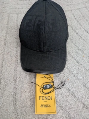 Fendi keps - Snygg svart keps från Fendi med det klassiska FF-logomönstret över hela kepsen. Böjd skärm med en stilren look och justerbar passform. Materialet ser ut att vara en mix av textil och läderdetaljer på skärmen. Perfekt för dig som gillar exklusiva accessoarer.