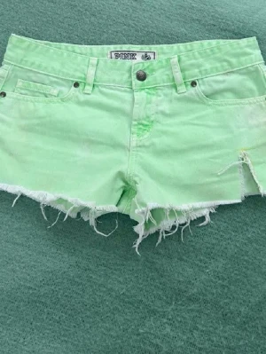 Ljusgröna jeansshorts från PINK lågmidjade low waist - Storlek 4 motsv S. Rakt över midjemått 39cm. Snygga ljusgröna jeansshorts från PINK Victoria's Secret med råa, fransiga kanter och klassisk femficksmodell. Shortsen har knapp och dragkedja framtill samt detaljerade sömmar.