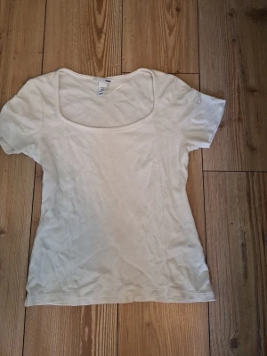 Vit kortärmad topp med rund hals - En enkel och stilren vit topp med korta ärmar och rundad, något djupare halsringning. Tillverkad i mjukt bomullsmaterial som känns skönt mot huden. Perfekt att matcha med jeans eller kjol för en clean look.