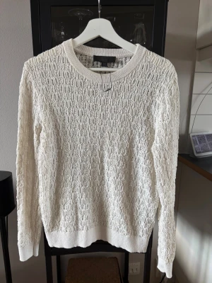 Vit stickad tröja från ZARA - Säljer en vit stickad tröja från ZARA med ett snyggt hålmönster över hela plagget. Tröjan har rund halsringning, långa ärmar och ribbade muddar vid ärmslut och nederkant. Perfekt för lager på lager och enkel att styla till olika looks.