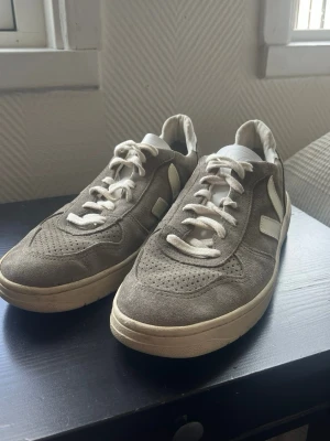 Veja V-10 sneakers i grå mocka - stl 42 - Veja V-10 sneakers i grå mocka, storlek 42 (US 9, UK 8). Mocka med off-white V-logga i läder.  Använda med synligt slitage: sulkanten är lite smutsig och mockan har mattats något på tåpartiet. Inga hål eller skador, sulmönstret är i stort sett intakt.  Rök- och djurfritt hem. Skriv gärna om du vill ha fler bilder eller undrar något!