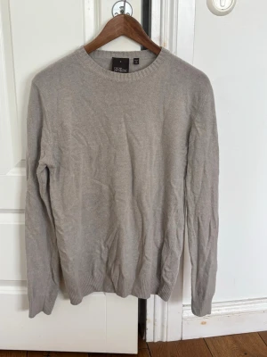 Beige stickad tröja Oscar Jacobson - Snygg beige stickad tröja från Oscar Jacobson, tillverkad i Italien. Tröjan har rund halsringning, ribbade muddar och är gjord i ett mjukt material som passar perfekt till lager på lager. Enkel och stilren design som funkar till det mesta.