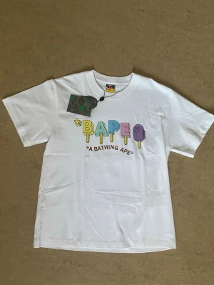 Vit Bape T-Shirt Popsicle Storlek S - Det här är en Bape Popsicle Tee ifrån säsongen summer/spring 2023, den är helt ny och har aldrig använts. Den kommer med alla tags som följer med vid köp. Den är perfekt för streetwear, vardags tröja eller så kan man ha den vid speciella tilfällen. Det är storlek S och den är True To Size. 