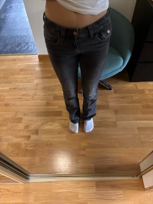 Mörkgrå bootcut jeans med broderad ficka - Säljer ett par mörkgrå bootcut jeans med snygg broderad detalj på bakfickan. Ena fickan saknar en knapp men annars är dom som nya! Är i barnstorleken 164 men ät ungefär som 34. 