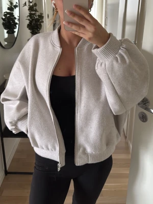Bomberjacka Zara - Säljer en ljusbeige bomberjacka i oversized modell med breda ärmar och ribbade muddar vid ärmslut och nederkant. Jackan har dragkedja framtill och är tillverkad i ett mjukt, filtliknande material. Perfekt för dig som gillar en avslappnad och trendig stil. Liten fläck på armen men går säkert bort 