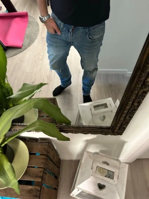 Blå slitna jeans med raka ben - Säljer ett par ljusblå jeans med slitningar och hål på knäna. Jeansen har raka ben, klassisk femficksmodell och normal midja. Perfekta för en avslappnad och trendig look. Materialet är denim i bomull.