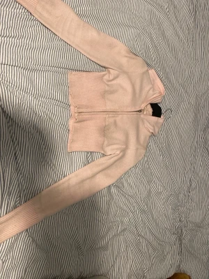 Ljusrosa ziptröja från Gina Tricot - Supersöt ljusrosa ziptröja från Gina Tricot med ribbade muddar och hög krage. Tröjan är stickad och har dragkedja framtill, perfekt för lager på lager och chill stil. Materialet känns mjukt och bekvämt mot huden.