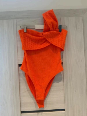 Magisk Orange Body - Säljer denna otroligt snygga body i en livlig orange färg. Den har en fantastisk asymmetrisk urringning där den är nästan off-shoulder på ena sidan, men har ett tjockt band/tygstycke över axeln på den andra.  • Skick: Endast använd en enda gång, så den är i absolut toppskick! • Märke: SHEIN. • Storlek: XS (EU 34).  • 🏠 Kommer från ett rök och djurfritt hem. • ⚡ Snabb leverans: Jag skickar inom 24 timmar!   