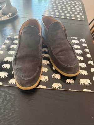 Mörkblå  loafers Loro Piana  - Säljer ett par stilrena mörkblå loafers i mocka med ljusbruna sulor. Skorna har en klassisk form utan snörning och är perfekta för dig som gillar en clean och avslappnad look. Passar till både jeans och chinos.