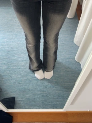 Svarta bootcut jeans med tryck - Säljer ett par svarta bootcut jeans med slitningar och ett coolt rosa tryck på bakfickan. Jeansen har en klassisk femficksmodell och är i stretchigt material för skön passform. Perfekta för dig som gillar en avslappnad men trendig stil.