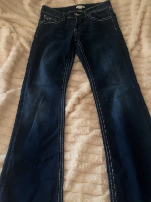 Mörkblå bootcut jeans med kontrastsömmar - Snygga mörkblå bootcut jeans med vita kontrastsömmar och klassiska fem fickor. Jeansen har ficklock med knapp bak och lätt utsvängda ben. Perfekta till en avslappnad och trendig look. Materialet är denim i bomull.