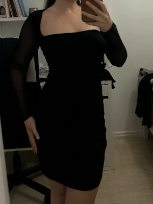 Svart kort klänning med meshärmar - Säljer en svart kort klänning med figurnära passform och långa meshärmar. Klänningen är tillverkad i ett stretchigt material som sitter tight mot kroppen. Size 34
