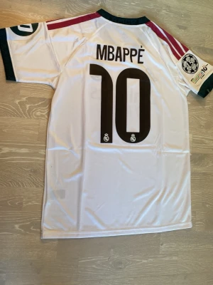 Real Madrid 26/27 mbappe  - Säljer en fet ny Real Madrid  T-shirt med Mbappe på ryggen.                                                                          Storlek är M och måtten finns på sista bilden.                         Den har aldrigs använts och är helt ny.                                  Priset kan diskuteras och skickar inom 24 Tim 💨☺️