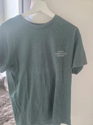 Grön t-shirt från Mads Nørgaard - Snygg grön t-shirt från Mads Nørgaard med diskret logga broderad på bröstet. Klassisk rund hals och korta ärmar. Perfekt basplagg i mjuk bomull som funkar till allt. Skulle kunna tänka mig att den passar ungdomar från åldern 13-16 år. 