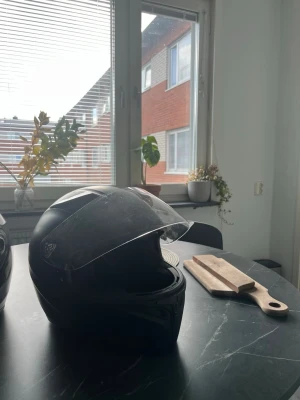 Svart Mc hjälm - Säljer en svart integralhjälm med genomskinligt visir. Hjälmen har en slimmad form och är tillverkad i hårdplast med mjuk stoppning på insidan. Perfekt för dig som kör motorcykel eller moped och vill ha bra skydd. Den är väldigt använd emd fungerar fortfarande utmärkt.