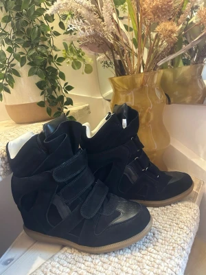 Isabel marant  - Snygga svarta sneakers med högt skaft och flera breda kardborreband. Skorna har en mix av mocka och läderdetaljer samt en ljusbrun sula. Insidan är ljus och skon har en chunky siluett som sticker ut.