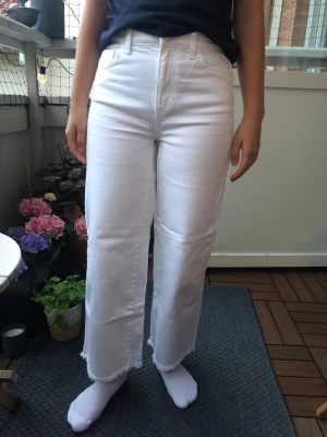 Vita raka jeans med rå kant - Säljer ett par vita jeans med rak passform och hög midja. Storleken är 158, men innerbenslängden är 62 cm och rakt över midjan är de 35 cm. Har inga fläckar eller andra skavanker.