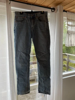 Blå raka jeans med fem fickor - Säljer ett par klassiska blå jeans med rak passform och fem fickor. Jeansen har en snygg tvättad look och stängs med dragkedja och knapp. Perfekta till en avslappnad stil och passar till det mesta i garderoben.