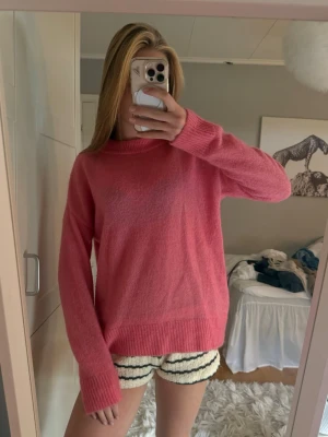 Rosa stickad tröja med rund hals - Mysig rosa stickad tröja med rund halsringning och långa ärmar. Tröjan har ribbade muddar vid ärmslut och nederkant, samt en avslappnad passform. Perfekt för lager på lager och enkel att styla till olika outfits.